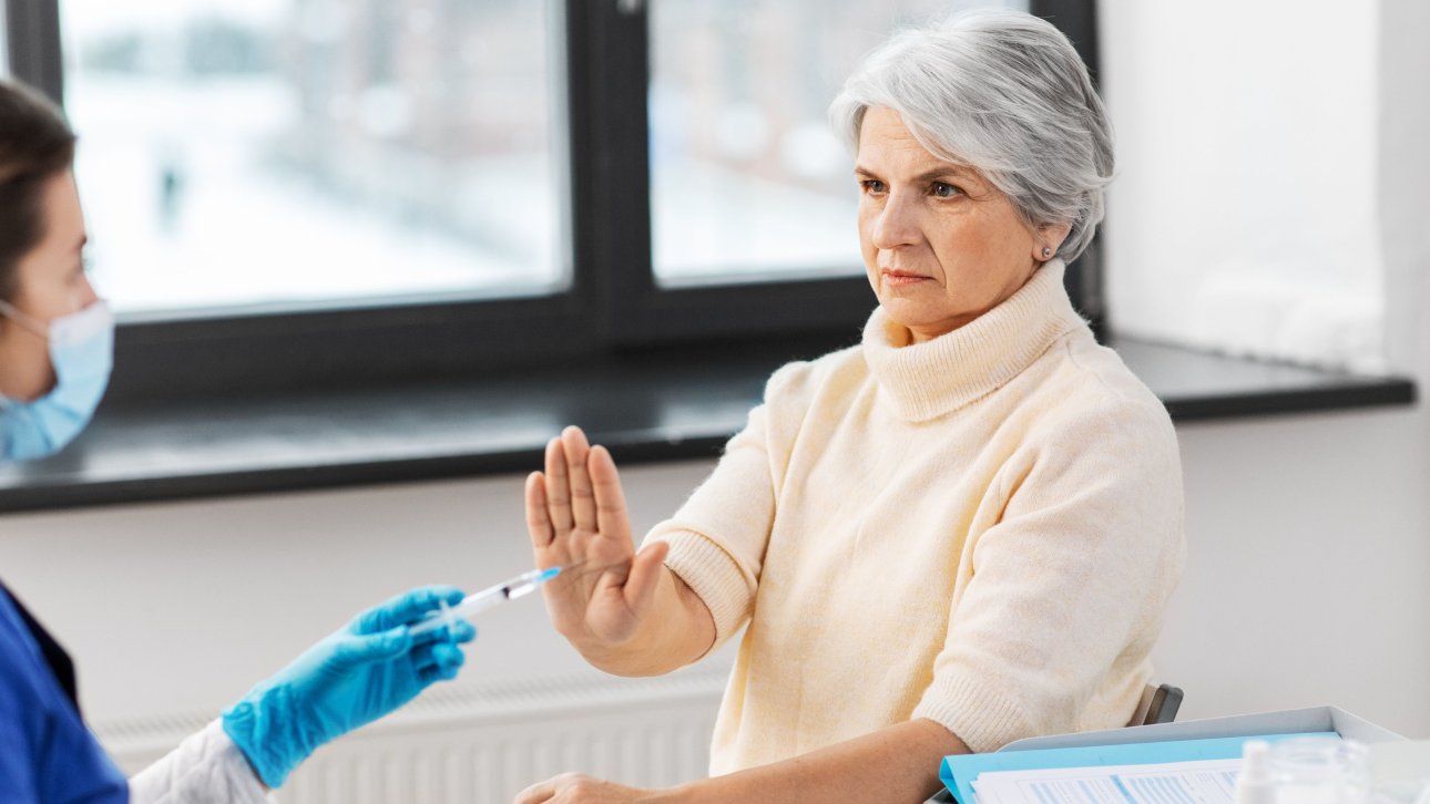 A woman waves her hand to refuse the injection a nurse is about to give her.