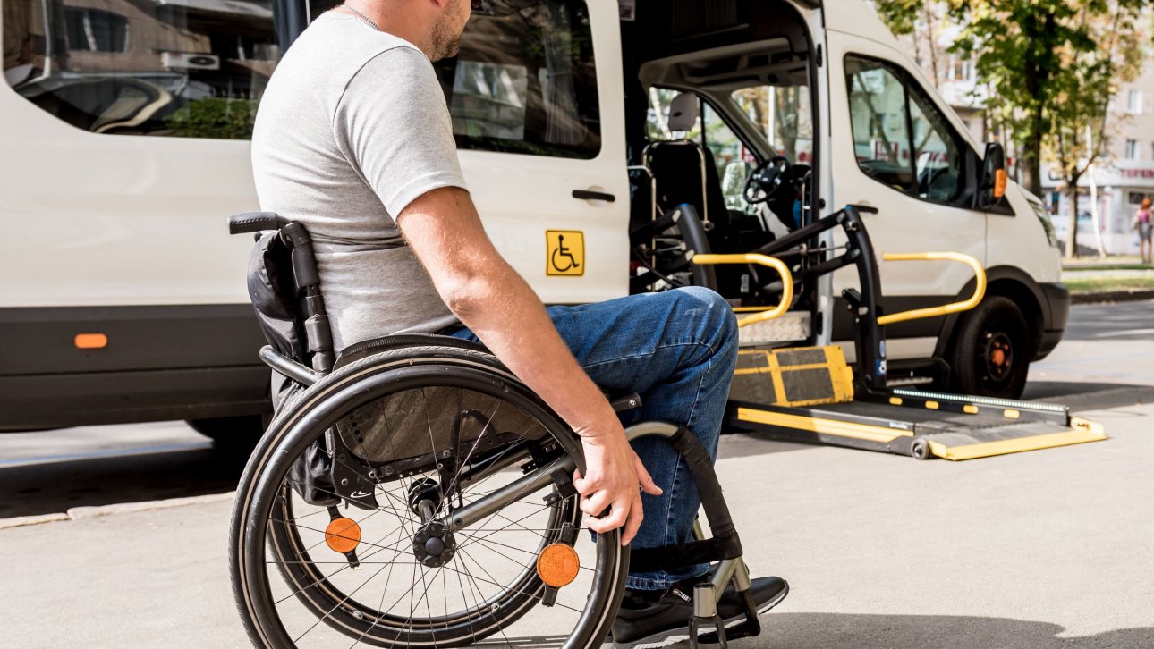 Un homme en fauteuil roulant regarde son transport adapté stationné dans la rue.