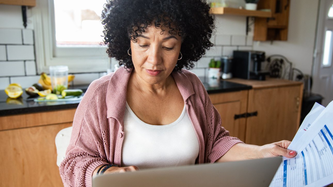 A woman looking at her computer whilst holding some papers in one hand.