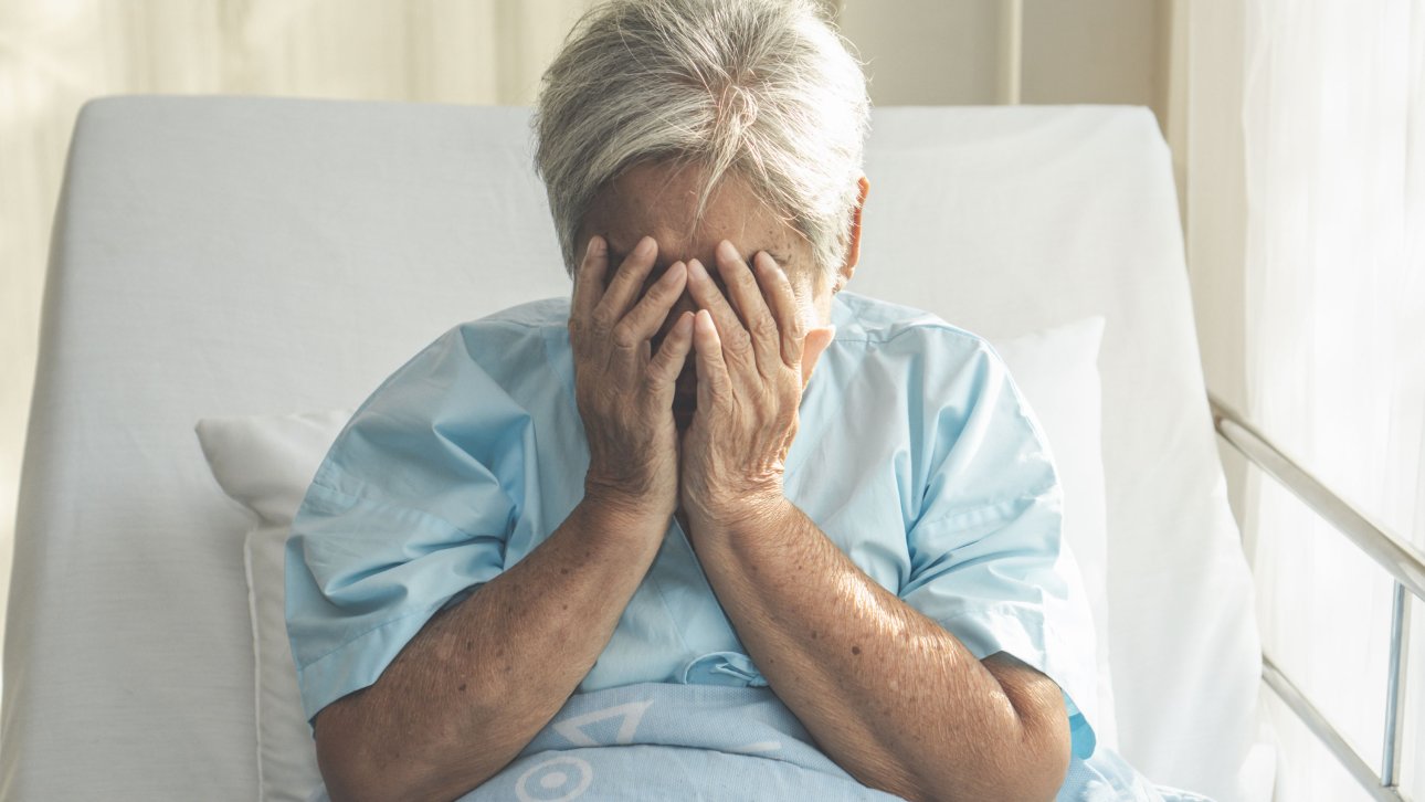 A patient sitting in a hospital bed, her face buried in her hands.
