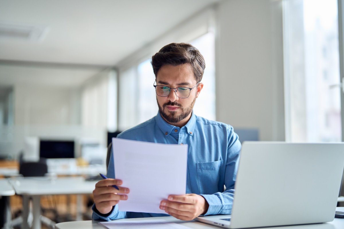 Enquêteur assis à son bureau devant son ordinateur portable et lisant un document.