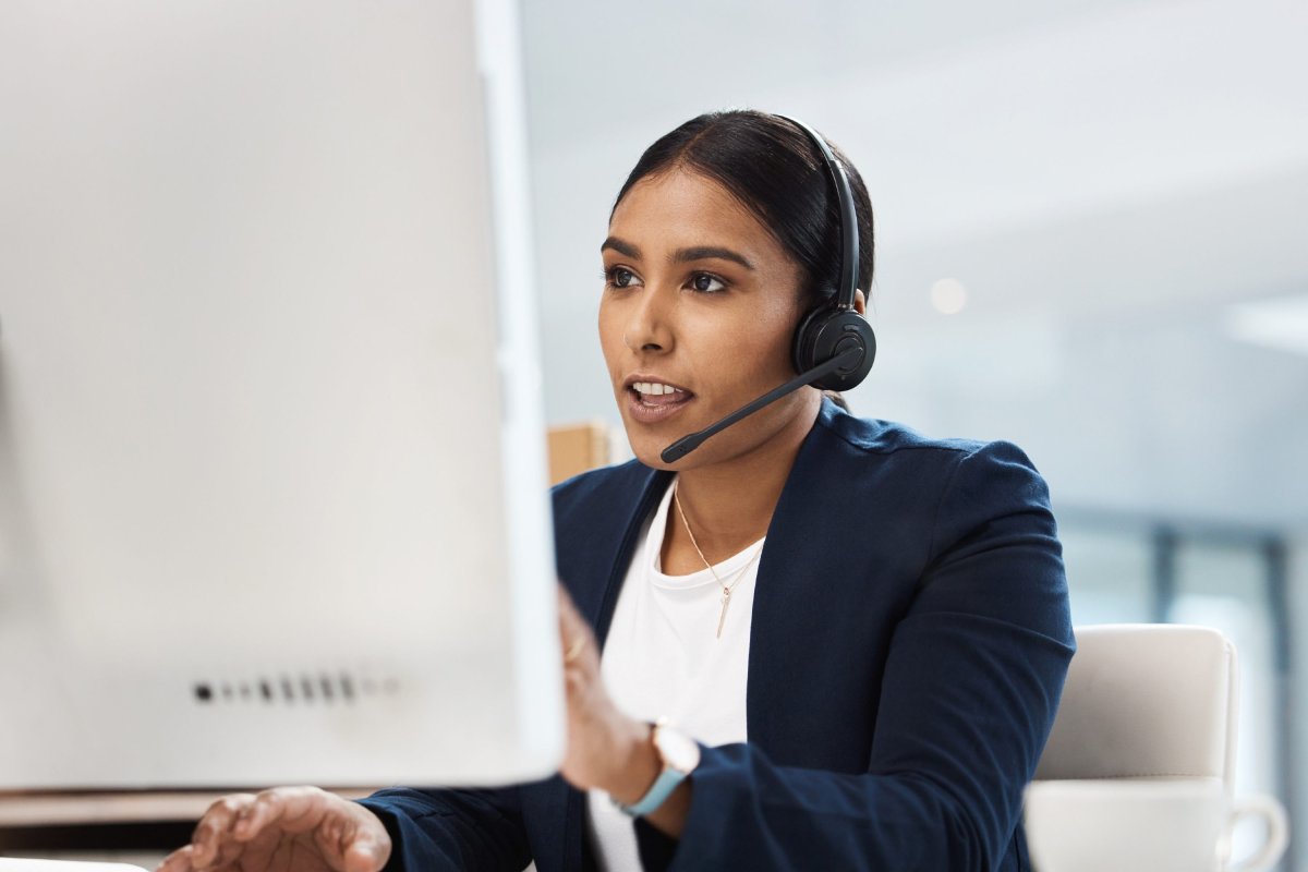 Enquêtrice assise à son bureau en regardant son écran d'ordinateur et en parlant dans son casque d'écoute.