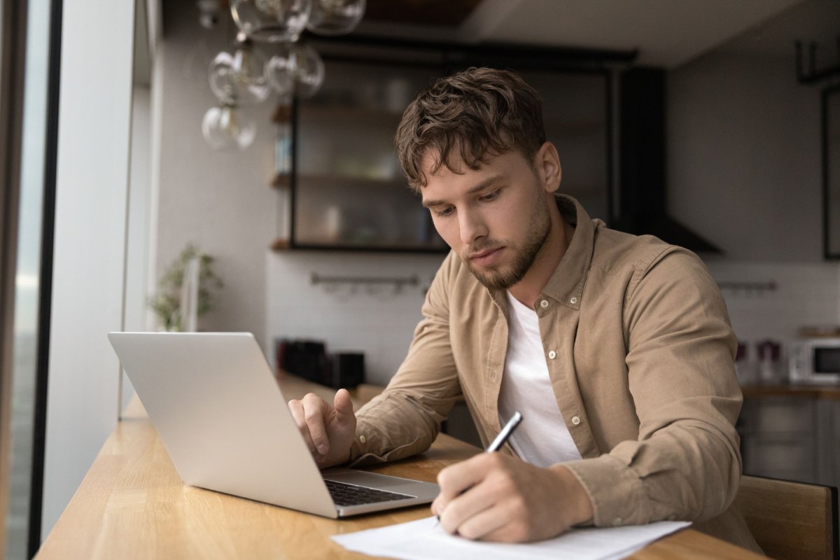 Un enquêteur assis devant son ordinateur portable prend des notes sur une feuille de papier.