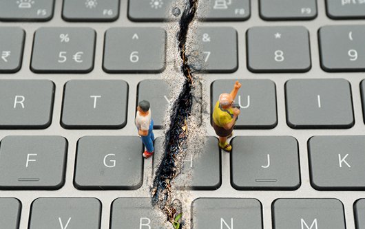Deux figurines posées sur un clavier d'ordinateur sont séparées par une profonde fissure.