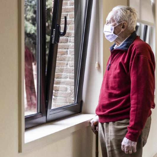 Elderly wearing a mask and looking out the window