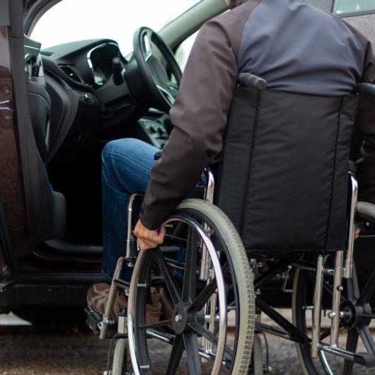 Homme en fauteuil roulant devant la porte ouverte d'une voiture