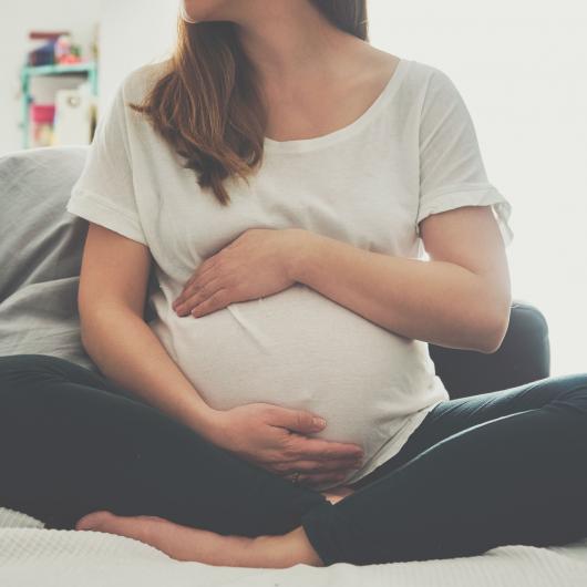 Femme enceinte assise sur un divan et tenant son ventre arrondi