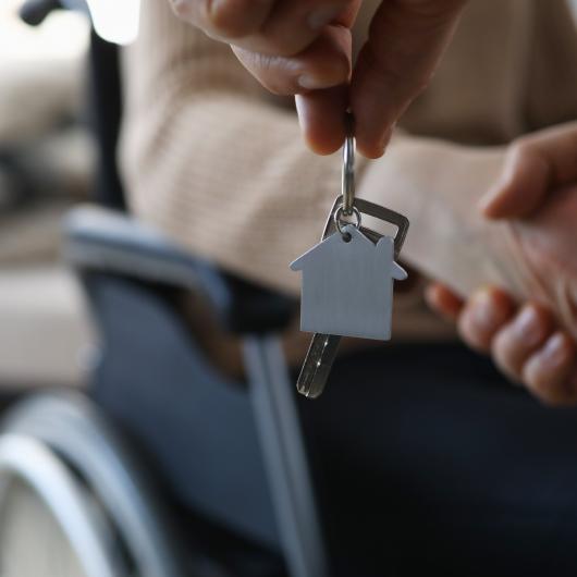 Porte-clé en forme de maison tendu devant une personne en fauteuil roulant