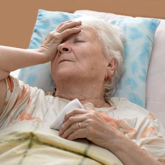 Dame âgée allongée dans un lit avec sa main sur son front