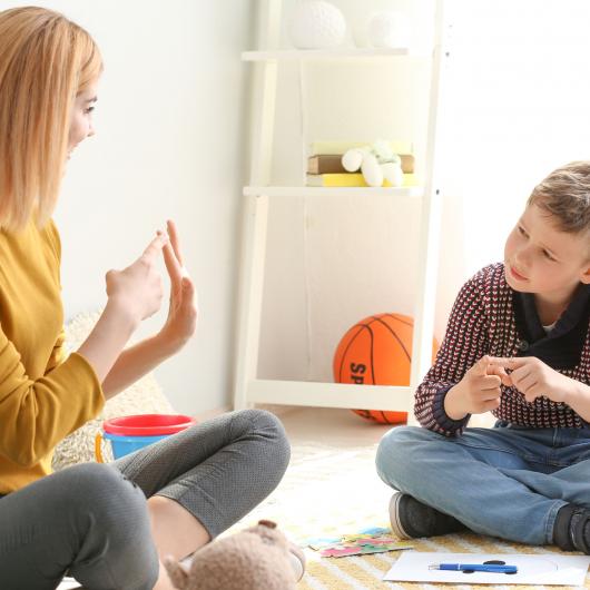 Female teacher showing fingers of her hand to a boy sitting on the floor