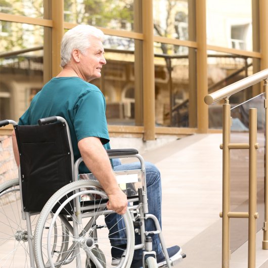 A man in a wheelchair in front of the access ramp to a private residence for seniors