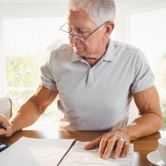 White-haired man using calculator in front of paper documents