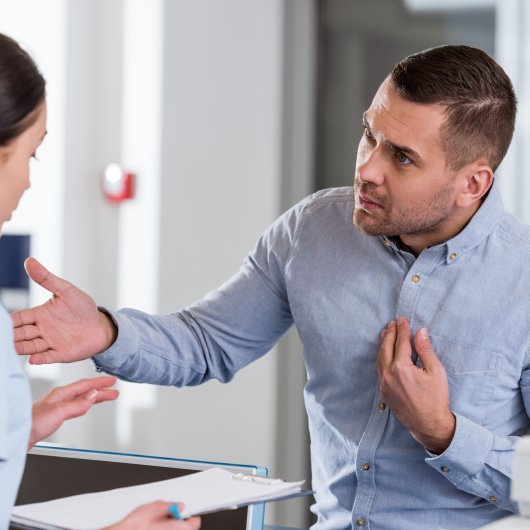 Dissatisfied man talking with the nurse who is behind the reception desk