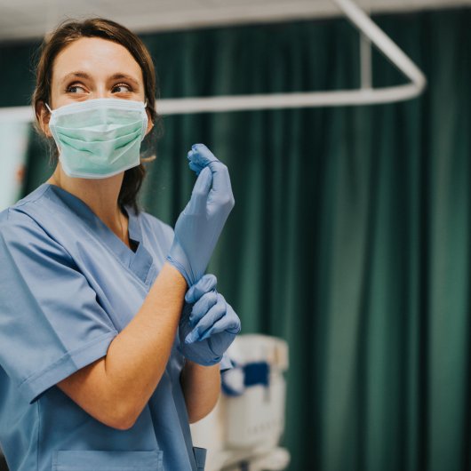 Une infirmière masquée qui retrousse son gant chirurgical