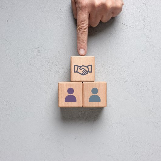 Two wooden blocks, each depicting a person, are placed under another block depicting a handshake.