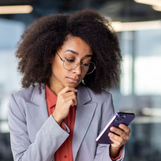 A professional employee looks doubtful while looking at her cell phone in the office.