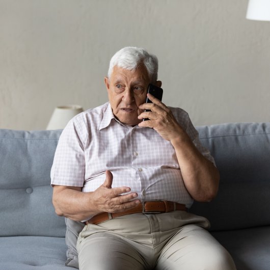 Elderly man sitting on his couch and chatting on the phone with a concerned look.