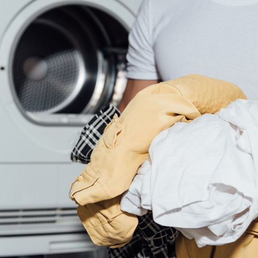 A man standing in front of a washing machine holds dirty clothes in his hands.