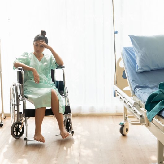 Upset young woman sitting in a wheelchair and wearing a hospital gown.