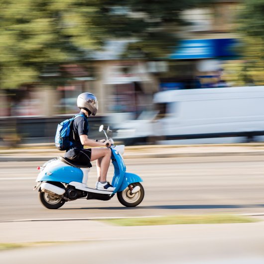 Adolescent conduisant un scooter sur la route.