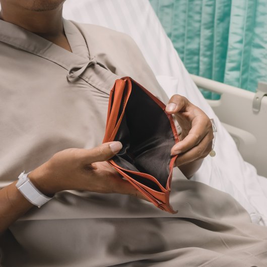 Patient couché sur un lit d'hôpital et montrant l'intérieur de son portefeuille vide.