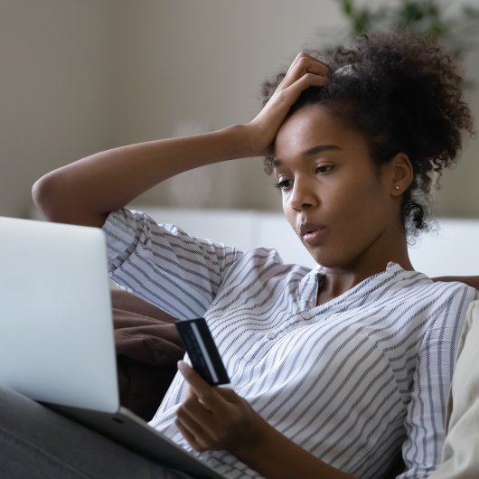 Jeune femme tenant sa carte de crédit en regardant son ordinateur portable d'un air confus.