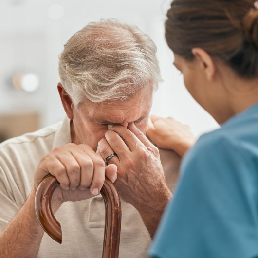 An old man holding his cane is comforted by a nurse.