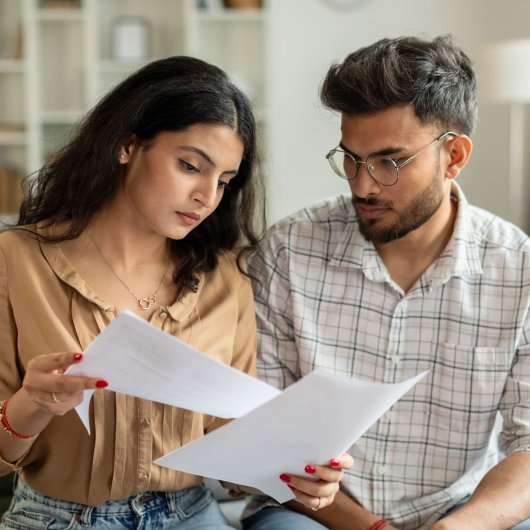 Jeune couple assis sur son divan et lisant une lettre.