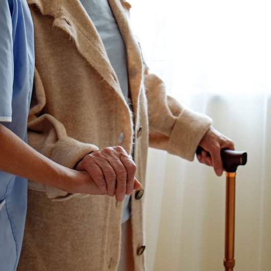 Home support worker helping an elderly woman to walk with her walking stick.