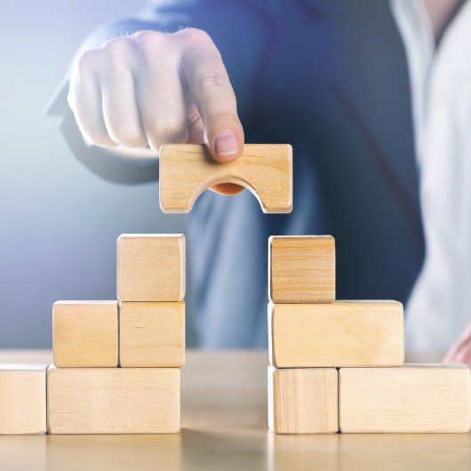 Hand placing a block in the shape of a bridge between two separate piles of blocks.