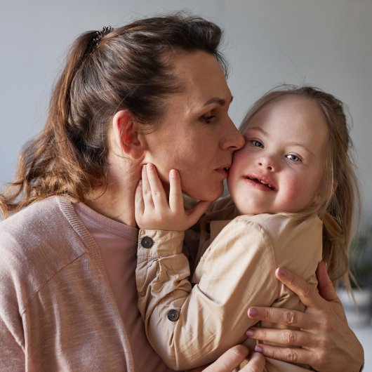 Mother kissing her daughter with Down syndrome on the cheek.
