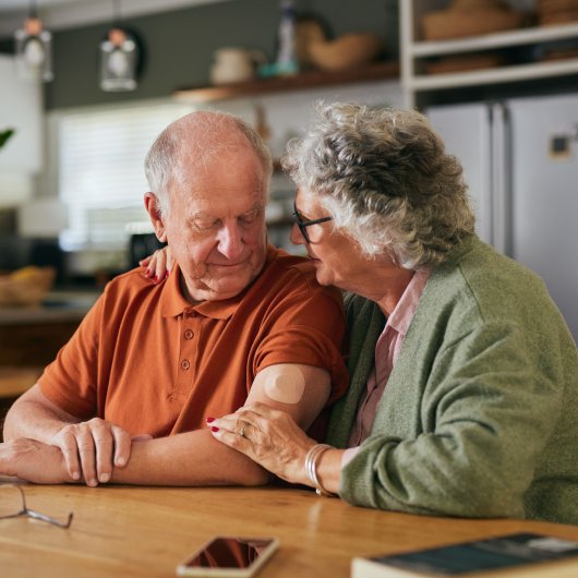 Une femme âgée touche le bras de son conjoint avec tendresse à la table de la cuisine.