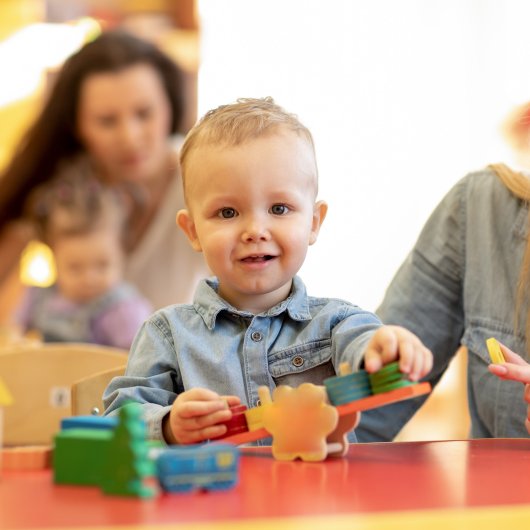 Petit garçon assis devant des jouets aux côtés de son éducatrice à la garderie ou au CPE.