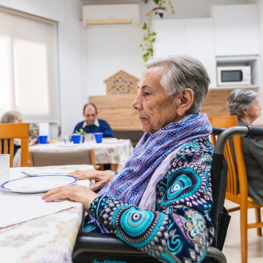 An elderly lady is sitting in front of an empty plate in a residential care home for the elderly.