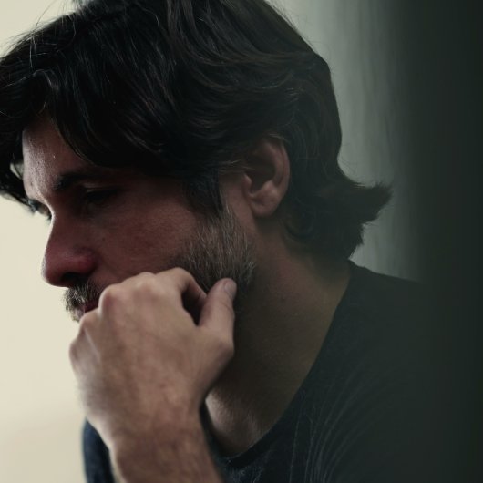 Visage d'un homme pensif dans une pièce sombre.