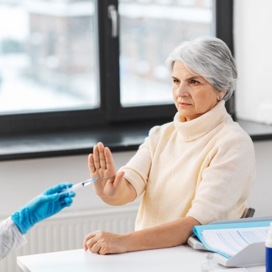 Une dame refuse de la main l'injection qu'une infirmière s'apprête à lui donner.