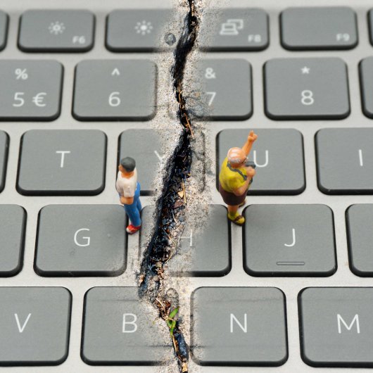 Deux figurines posées sur un clavier d'ordinateur sont séparées par une profonde fissure.