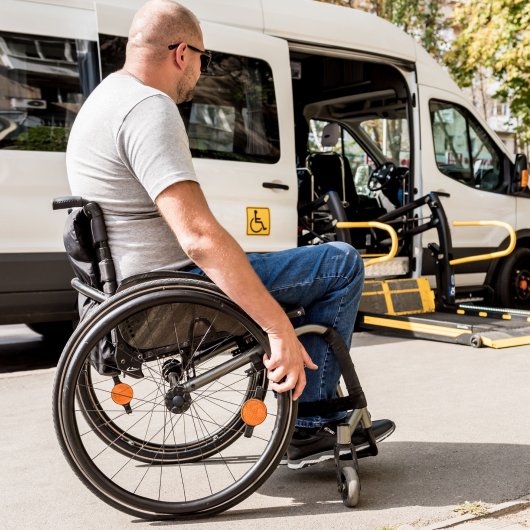 Un homme en fauteuil roulant regarde son transport adapté stationné dans la rue.