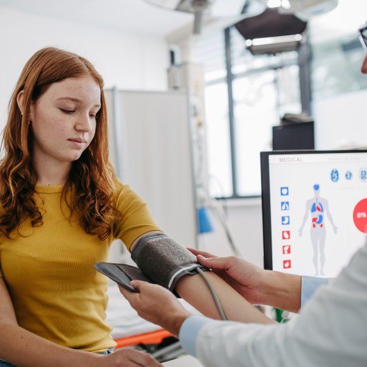 Une adolescente fait prendre sa pression par un médecin.