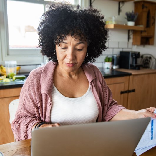 Femme consultant son ordinateur en tenant des papiers dans une main.