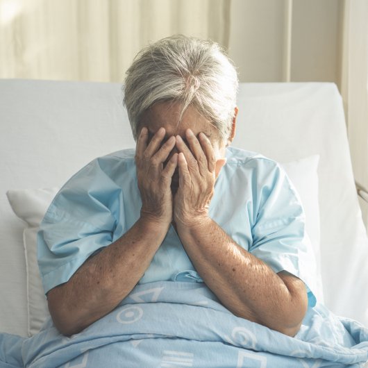 Patiente assise dans un lit d'hôpital, le visage enfoui dans ses mains.